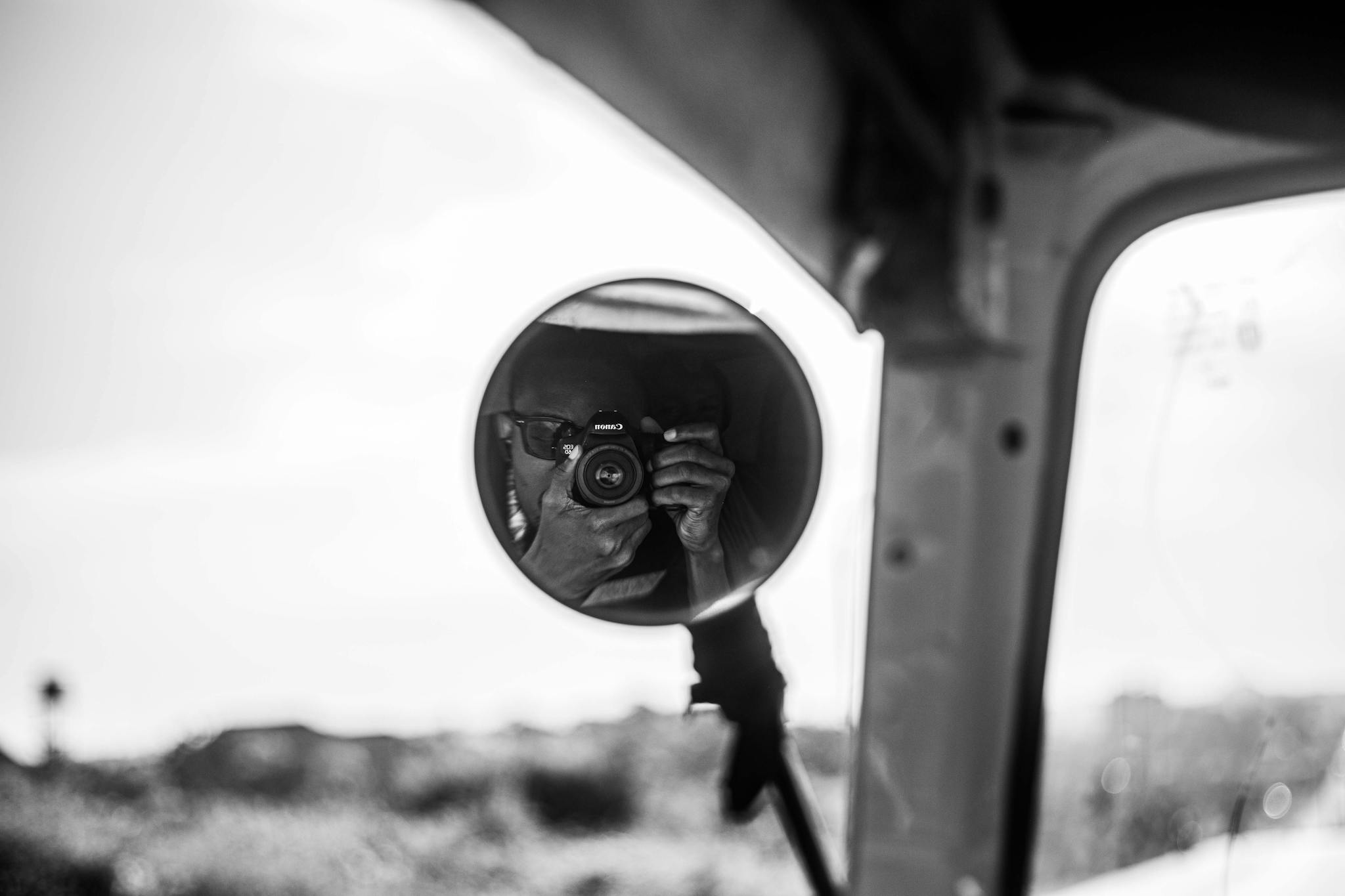 A monochrome reflection of a photographer in a car's side mirror, capturing the moment.